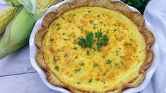 a quiche with parsley in a white dish next to corn on the cob