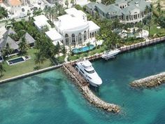 an aerial view of a yacht docked in the water near a large house and palm trees