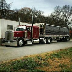 a red semi truck driving down a road next to a white trailer house and trees