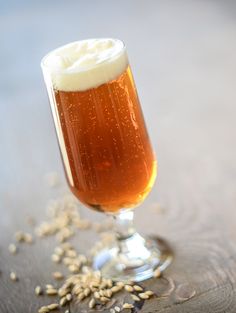 a glass filled with beer sitting on top of a wooden table next to grains