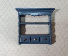 a blue shelf with two drawers on it against a wallpapered background that looks like an ornament