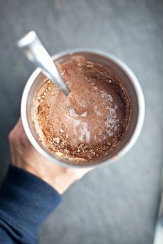 a person holding a cup with some kind of substance in it and a spoon sticking out of the top