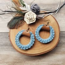 a pair of blue crochet hoop earrings sitting on top of a wooden board