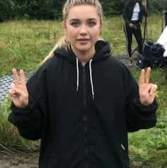 a woman in a black jacket is making the peace sign with her hands and two other people behind her