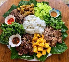 a platter filled with meat, vegetables and sauces on top of a wooden table