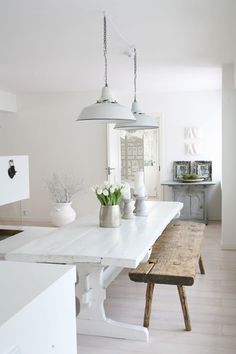 a white table and bench in a room with wood flooring, two lights hanging from the ceiling