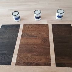 three paint cans sitting on top of a wooden floor next to two different colors of wood