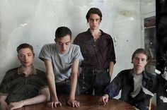 a group of people sitting around a wooden table in front of a wall with peeling paint on it