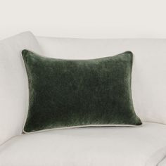 a green velvet pillow sitting on top of a white couch