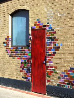 a red door is in front of a brick wall with colorful tiles on the side