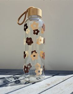 a clear bottle with brown and white flowers on it sitting on top of a wooden table