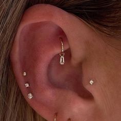 a woman's ear is adorned with tiny diamond studs and gold hoop earrings