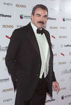 a man in a tuxedo and bow tie poses for the camera on the red carpet