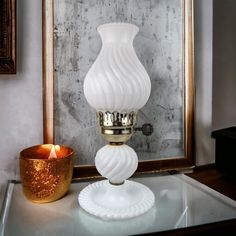 a white glass vase sitting on top of a table next to a gold candle holder