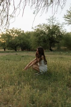 a woman sitting in the grass with her legs crossed and looking up at something behind her