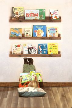 a little boy laying on the floor reading a book in front of bookshelves