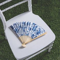 a blue and white fan sitting on top of a white chair with grass in the background