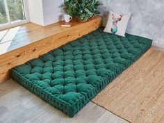 a green futon bed sitting on top of a wooden floor next to a window