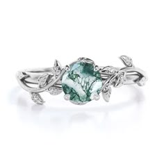 a white gold ring with green and white stones on the side, surrounded by leaves