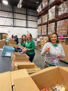 three women are standing in a warehouse with boxes on the floor and one woman is holding something