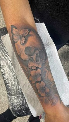 a skull with flowers and butterflies on it's arm is seen in this image