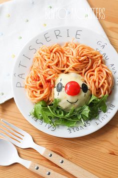 a white plate topped with spaghetti and a clown face on top of it next to silverware