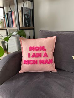 a pink pillow that says mom, i am a rich man on the back of a couch