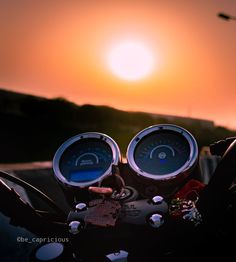 two gauges on the handlebars of a motorcycle at sunset in front of an orange sky