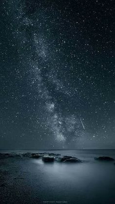 the night sky is filled with stars and some rocks in the water, as well as an airplane flying overhead