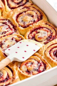 a pan filled with cinnamon rolls and a spatula on top of the baking dish