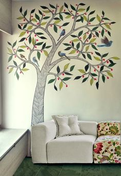 a white couch sitting under a tree painted on the side of a wall next to a window