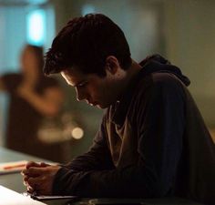 a young man sitting at a table writing on a piece of paper