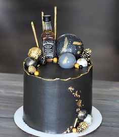 a black cake with gold decorations and a bottle of whiskey on top is sitting on a wooden table