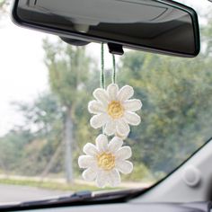 two white crocheted flowers hanging from a car's rear view mirror frame