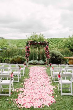 an outdoor ceremony with white chairs and pink petals on the aisle leading up to it