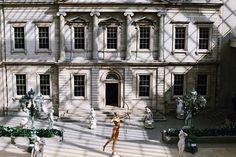 an old building with statues in front of it and people walking around the courtyard area