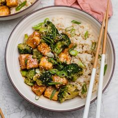 two bowls with rice, broccoli and tofu on them next to chopsticks