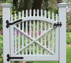 a white gate with two black handles on the top and bottom, in front of some flowers