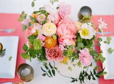 an arrangement of flowers in a white vase on a pink table cloth with silverware