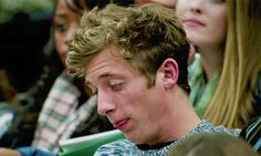 a young man is looking at his cell phone while sitting in a crowd with other people