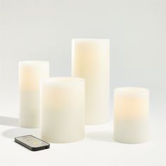 three white candles and a cell phone on a table