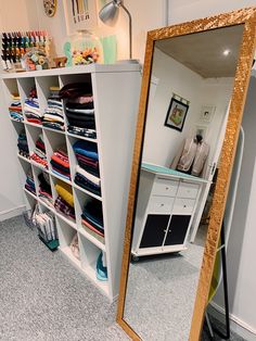 a large mirror sitting on top of a floor next to a shelf filled with clothes