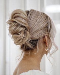 a woman with blonde hair in a low bun updo, wearing gold earrings and a white dress