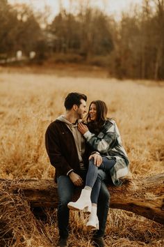 a man and woman are sitting on a log in the middle of an open field