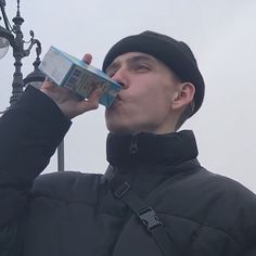 a man in black jacket drinking out of a blue box next to a street light