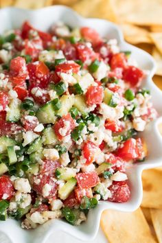 a white bowl filled with cucumber, tomato and feta salad next to chips