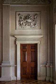 an empty room with two wooden doors and ornate carvings on the wall above it is a checkered floor