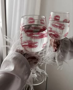 two wine glasses with red lipstick painted on them are held by someone's hand