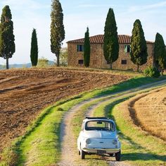 an old car is parked on the side of a dirt road in front of some trees