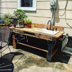 a sink sitting on top of a wooden table next to a chair and potted plant